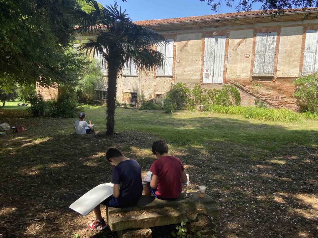 Enfants participant à un cours de dessin en extérieur à Aureville, initiation au carnet de voyage et au patrimoine, animé par Audrey Bourdin de l'Atelier Pieko à Toulouse
